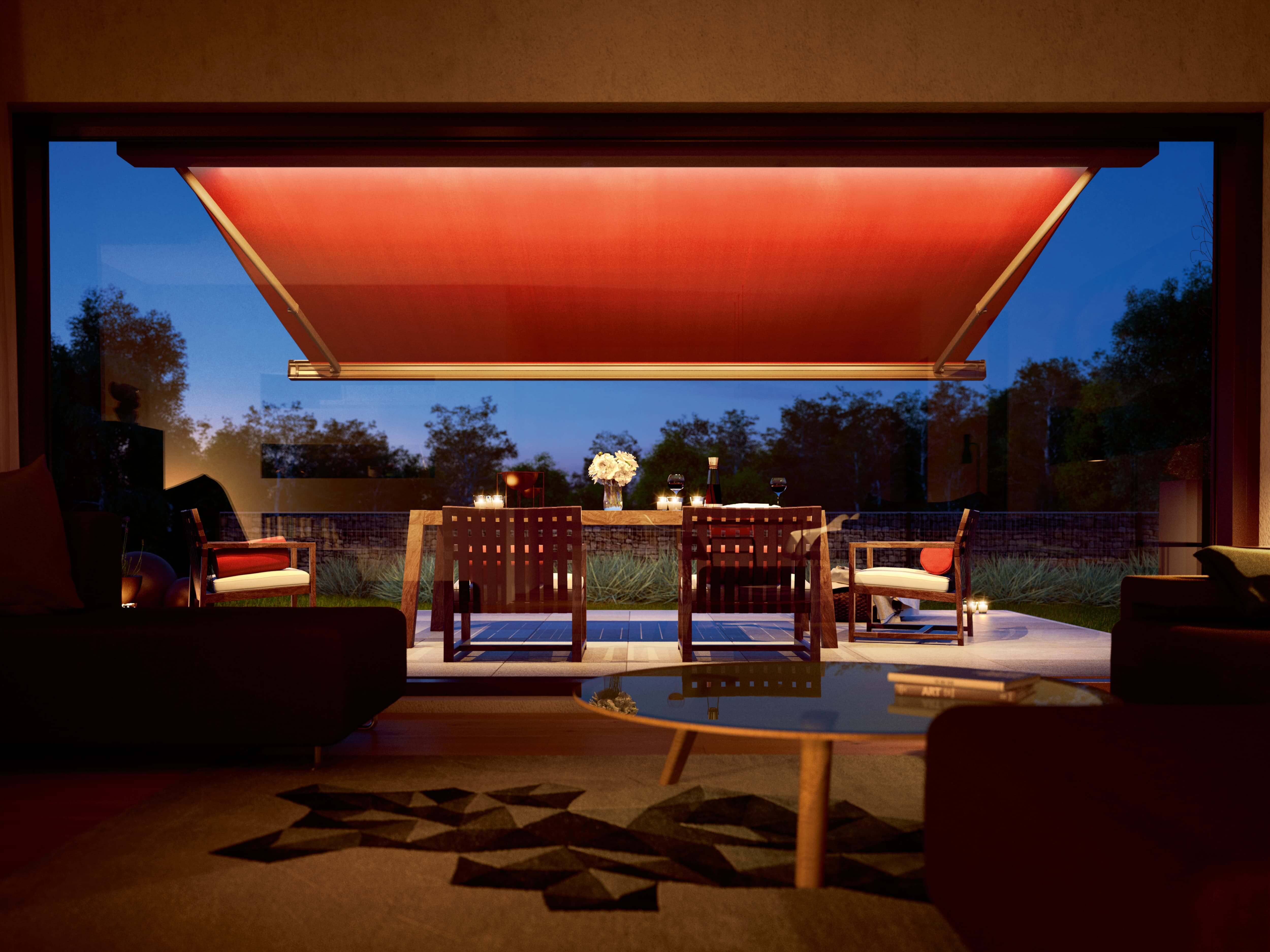 Stilvolle Terrasse am Abend mit einer beleuchteten Markise. Die Markise hat LED Beleuchtung im Kasten, so dass die eingerichtete Terrasse darunter beleuchtet ist.