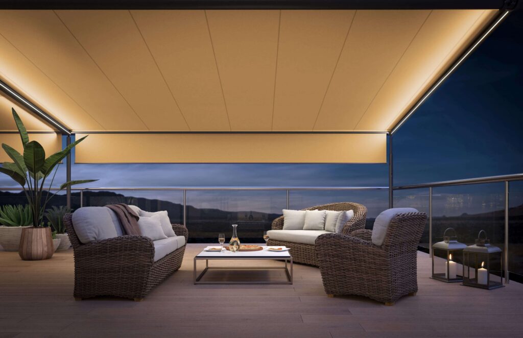 Stilvolle Terrasse am Abend. Die ausgefahrene Pergola Markise hat LED Beleuchtung in den seitlichen Führungsschienen und beleuchtet die Terrasse.