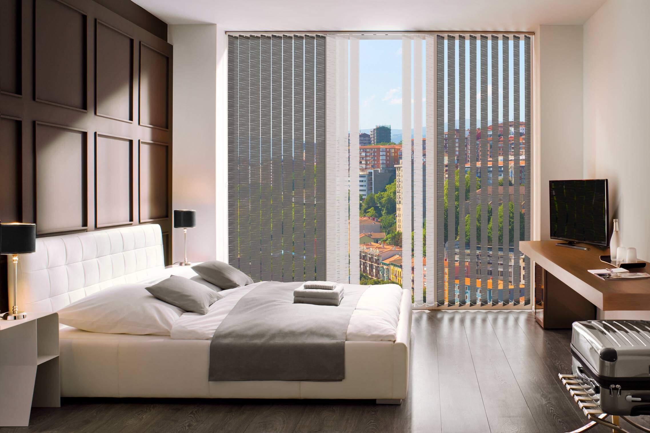 Hotelzimmer mit einem großen Bett mit einer großen Glasfront. Vorderglasfront sind Lamellenvorhänge montiert worden. Diese sind in der Mitte weiß und außen grau