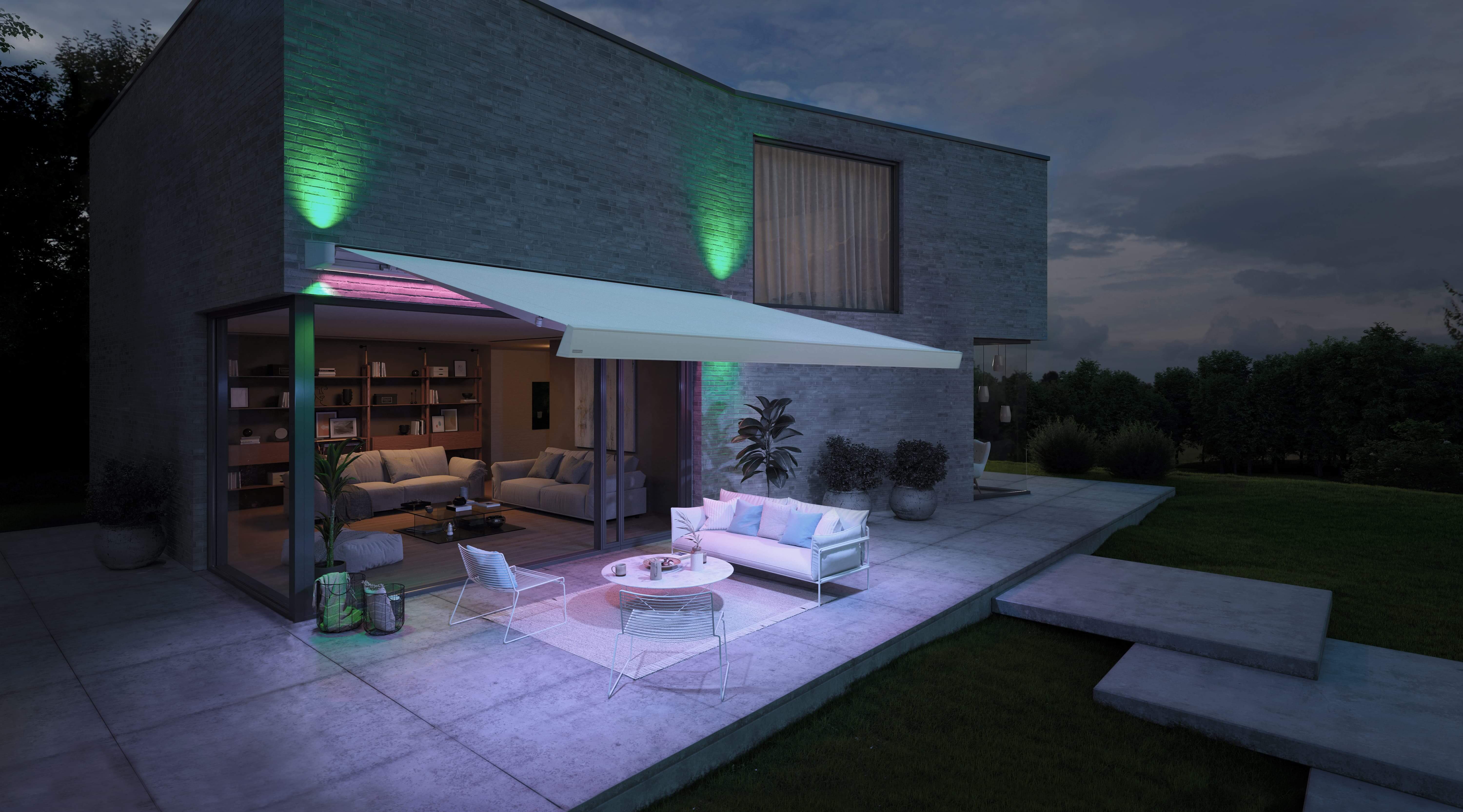 Stilvolle Terrasse eines Einfamilienhauses mit einer ausgefahrenen Markise, die LED Beleuchtung hat. Die LED Beleuchtung hält die Terrasse in einem stimmungsvolles Licht.