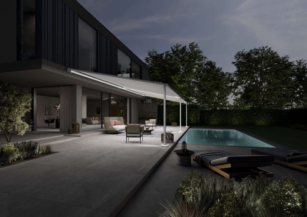 Seitlicher Ansicht einer Terrasse mit Pool. Die ausgefahrene Pergola Markise hat LED Beleuchtung im Kasten in den Führungsschienen und in der Säule, so dass die Terrasse gut ausgeleuchtet wird.