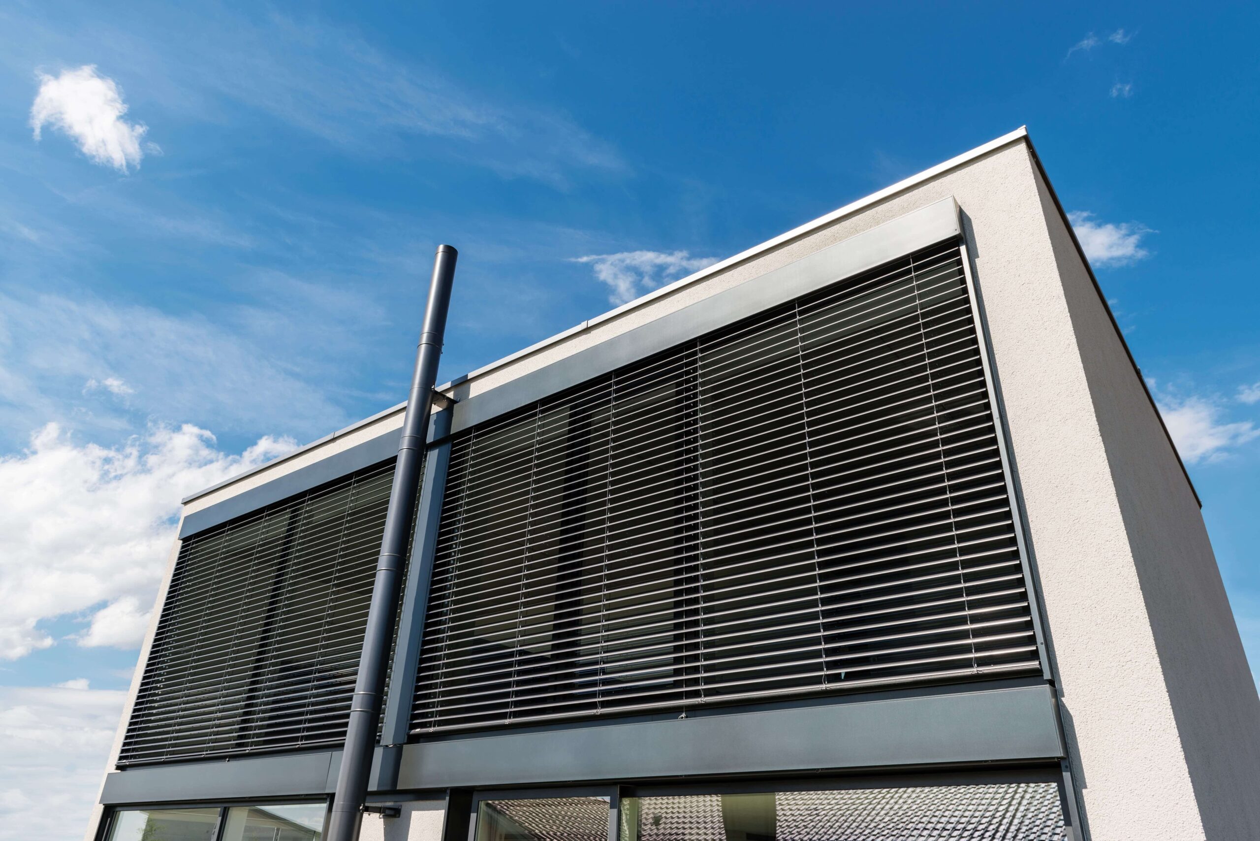 Außenansicht eines modernen Hauses mit einer großen Glasfront an dem große Raffstore zur Beschattung montiert sind.