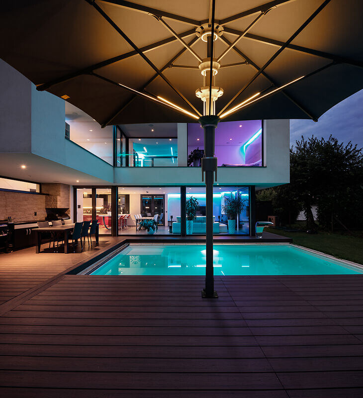 Terrasse am Abend mit Pool und einem Sonnenschirm mit LED Beleuchtung