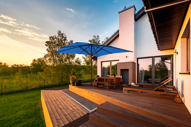 Terrasse eines Einfamilienhauses mit Gartenmöbeln und einem blauen rechteckigen Sonnenschirm